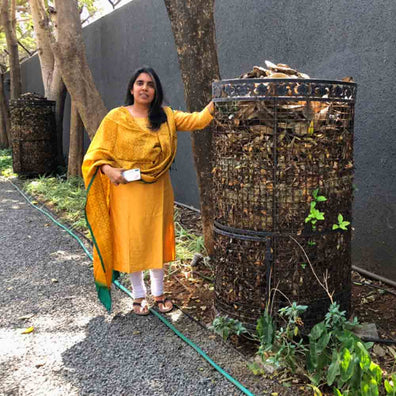 Lady standing next to Daily Dump metal leaf composter 32inches lined up in outddoor landscaped area